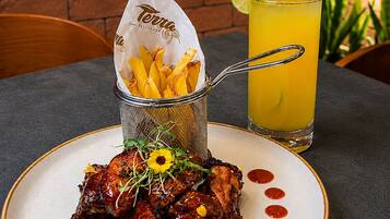 A plate of glazed chicken wings with a side of fries and a glass of yellow beverage on a table.