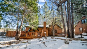 A cabin with a wooden deck, surrounded by trees and snow.