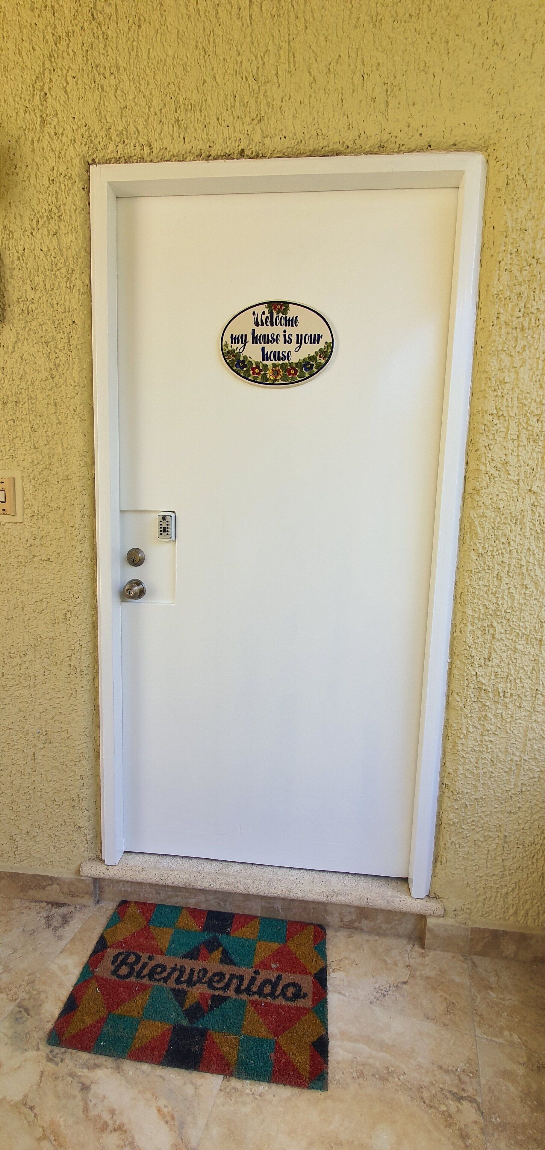 A white door with a welcome sign and a colorful mat.
