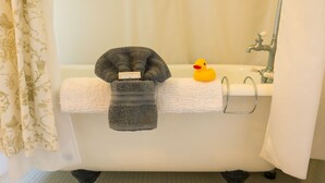 A bathtub with a white towel and a gray towel draped over it, a yellow rubber duck, and a metal faucet.