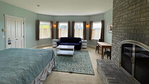A room with a bed, a sofa, a small table, a fireplace, and large windows.