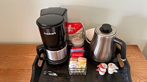 A coffee maker, a stainless steel pot, a box of Stash coffee pods, a jar of sugar, a jar of creamer, and a bottle of milk on a black tray.