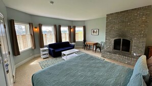 A bedroom with a large bed, a blue sofa, a small table, a fireplace, and a window with curtains.
