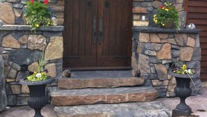 A stone entrance with a wooden door, two lantern-style lights, and flower planters. - One Of A Kind Mountain Home With Gorgeous  mountain Views  (Canmore)