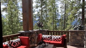 An outdoor deck with a stone wall, wooden furniture, and a view of trees and mountains. - One Of A Kind Mountain Home With Gorgeous  mountain Views  (Canmore)