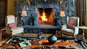 A stone fireplace with a lit fire, flanked by two chairs and a table with a vase. - One Of A Kind Mountain Home With Gorgeous  mountain Views  (Canmore)