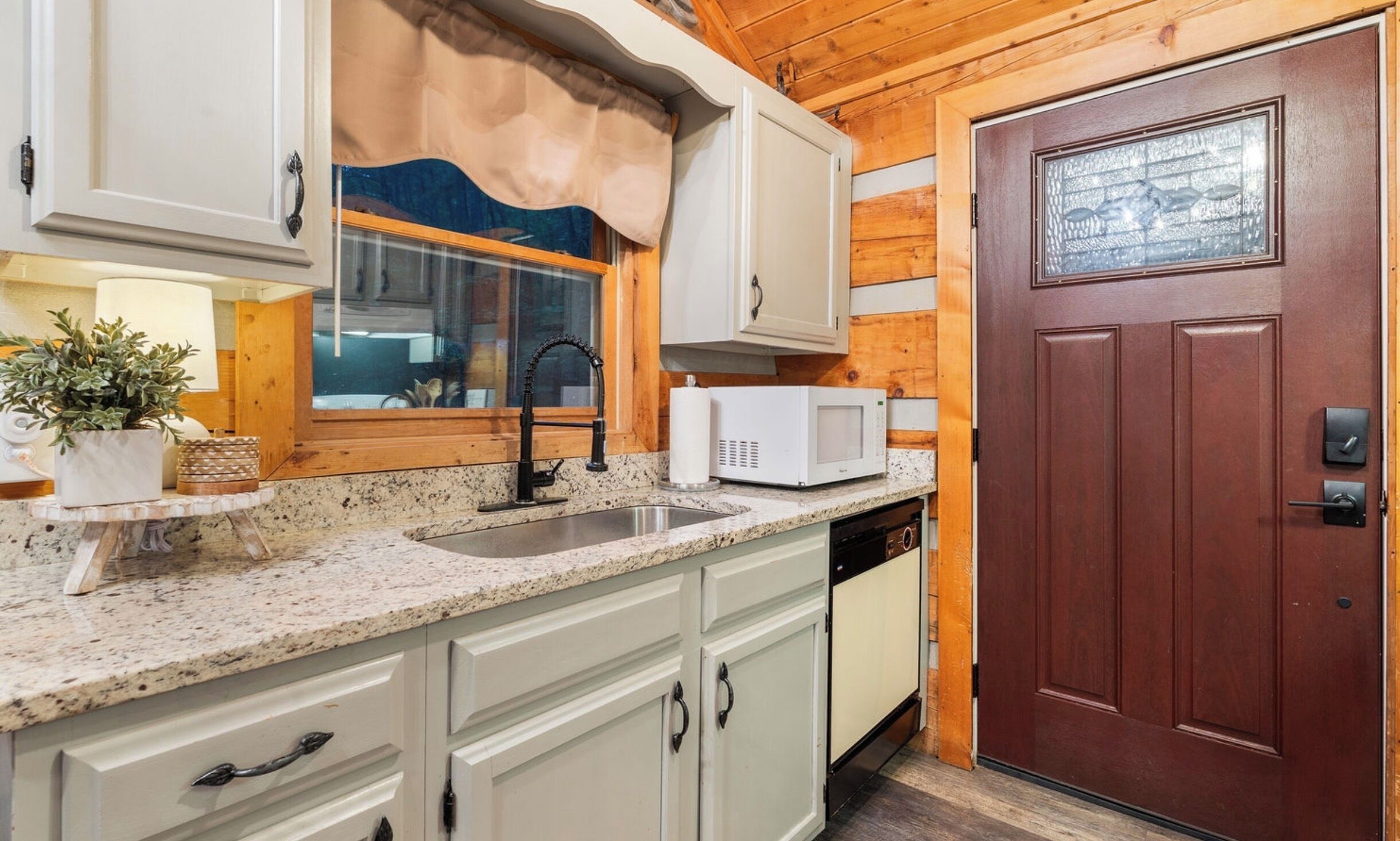 A kitchen with white cabinets, a granite countertop, a microwave, and a wooden door.