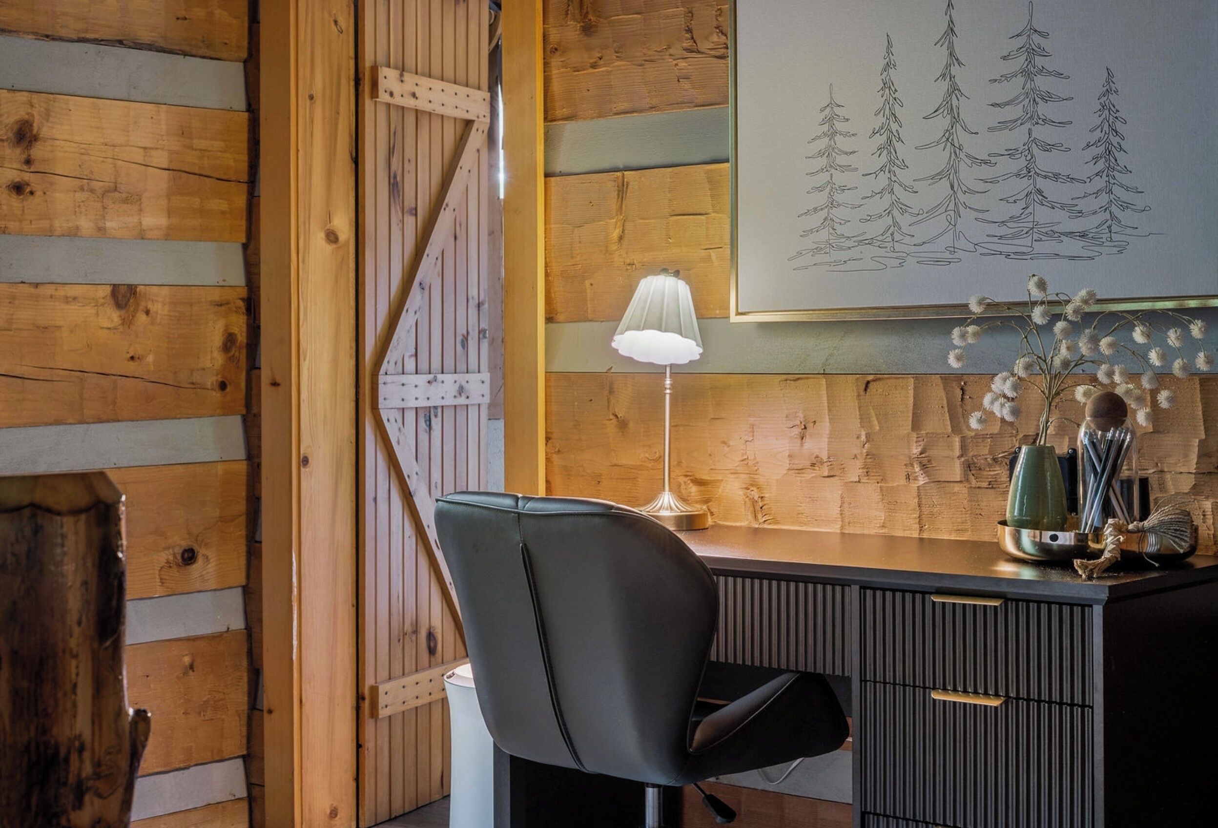 A wooden interior with a desk, chair, lamp, and a wall art of trees.
