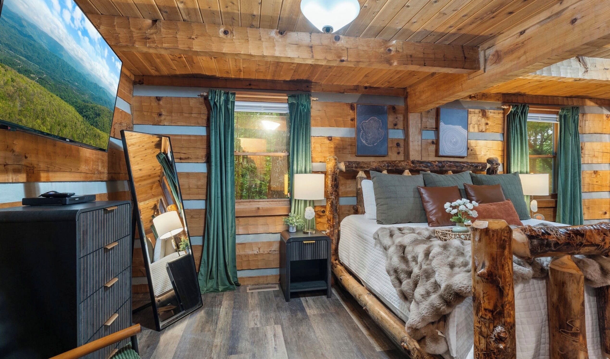 A log cabin bedroom with a bed, bedside tables, a dresser, and a mirror.