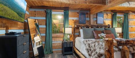 A log cabin bedroom with a bed, bedside tables, a dresser, and a mirror.