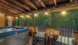 A wooden cabin with a hot tub, two chairs with striped cushions, and a forest view through large windows. - 🔥 Hot Tub Cabin Near Parkway King Suite + Pet Friendly (Sevierville)