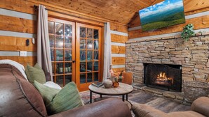 L’intérieur d’un chalet confortable, avec une cheminée en pierre, des murs en bois et une grande fenêtre agrémentée de rideaux.