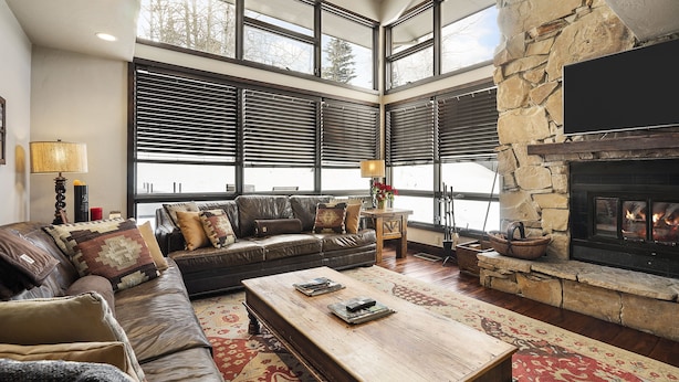 A cozy living room with a stone fireplace, leather sofa, and large windows.