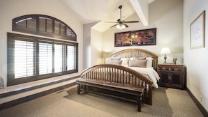 A bedroom with a large window, a bed with a wooden headboard, a nightstand, and a ceiling fan.