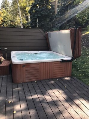 Relax in a hot tub on a secluded outdoor deck surrounded by trees.
