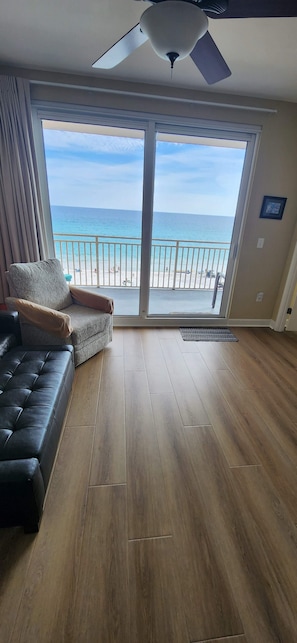 A room with a large sliding glass door leading to a balcony with a view of the beach.