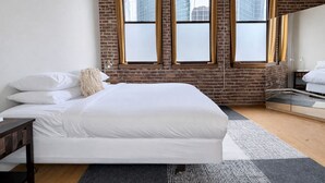 Ein modernes Schlafzimmer mit einem großen Bett, einer Ziegelwand und einem Blick auf die Stadt durch große Fenster.