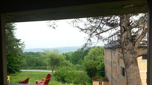 Une vue depuis un porche doté d’une balustrade en bois, donnant sur une zone herbeuse avec un petit bâtiment et des arbres.