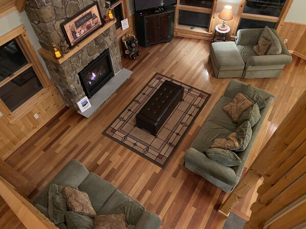 A cozy living room with a stone fireplace, two green sofas, a coffee table, and a TV. - True North at Sunday River-Powder Ridge-4miles to Mtn. New Air Conditioning !! (Newry)