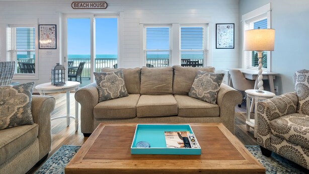 Ein Wohnzimmer mit einem beigefarbenen Sofa, einem Couchtisch mit einer Zeitschrift und Meerblick durch große Fenster.