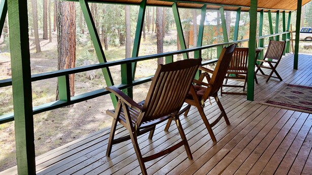 A covered wooden deck with two rocking chairs facing a forested area.