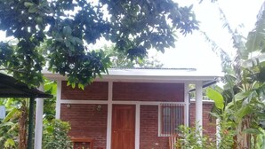 Una casa de ladrillo de dos pisos con puerta y ventana de madera, rodeada de abundante vegetación.