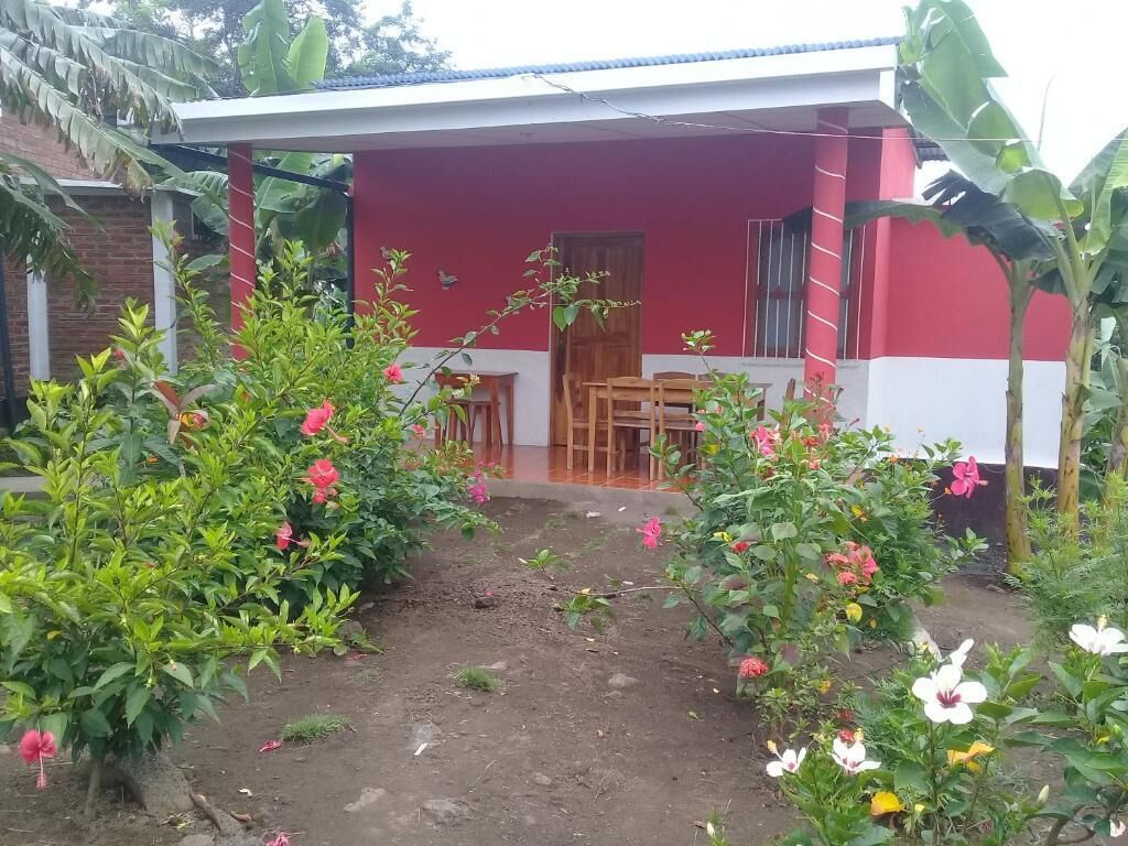 Un bâtiment rouge doté d’un porche abrité, entouré de plantes en fleurs et d’un petit jardin.