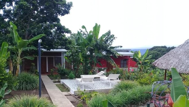 Un jardín con un sendero que lleva a una zona de estar con sillas blancas y una estructura de techo de paja.