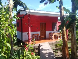 A red and white building with a wooden door, a small table, and chairs outside. - Inn Hospedaje BullShark (Altagracia)