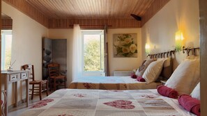 Une chambre avec deux lits, un bureau, une chaise et une fenêtre donnant sur des arbres.