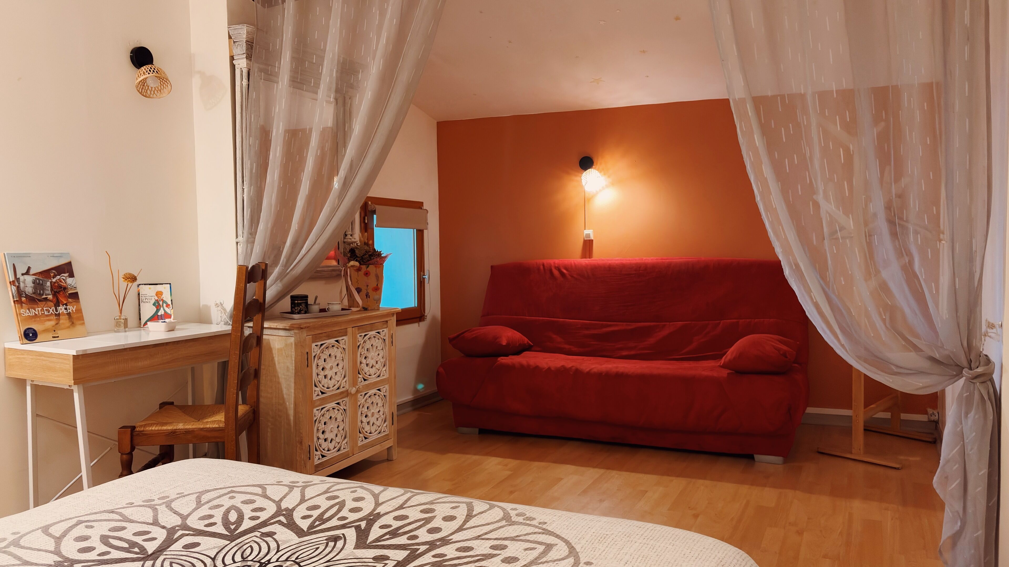 Une chambre à coucher avec un bureau en bois, un canapé rouge, une couvre-lit à motifs et une table de chevet avec une lampe.