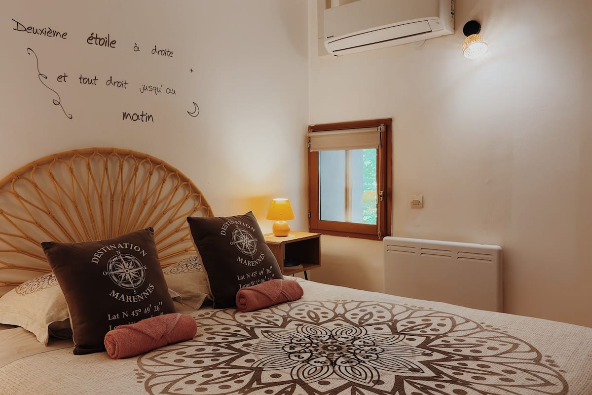 A bedroom with a large bed, a wall with a quote, a window, and a bedside lamp.