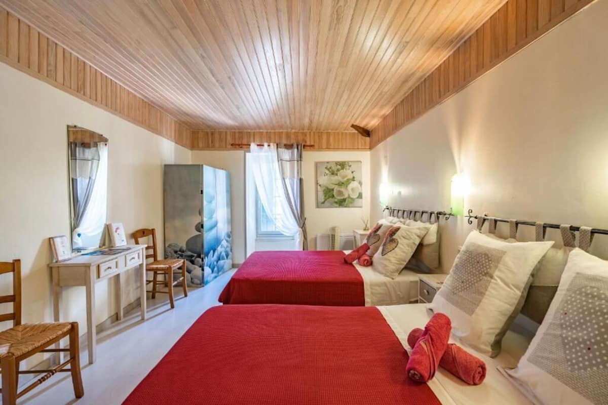 A room with two beds, a desk, chairs, and a painting.