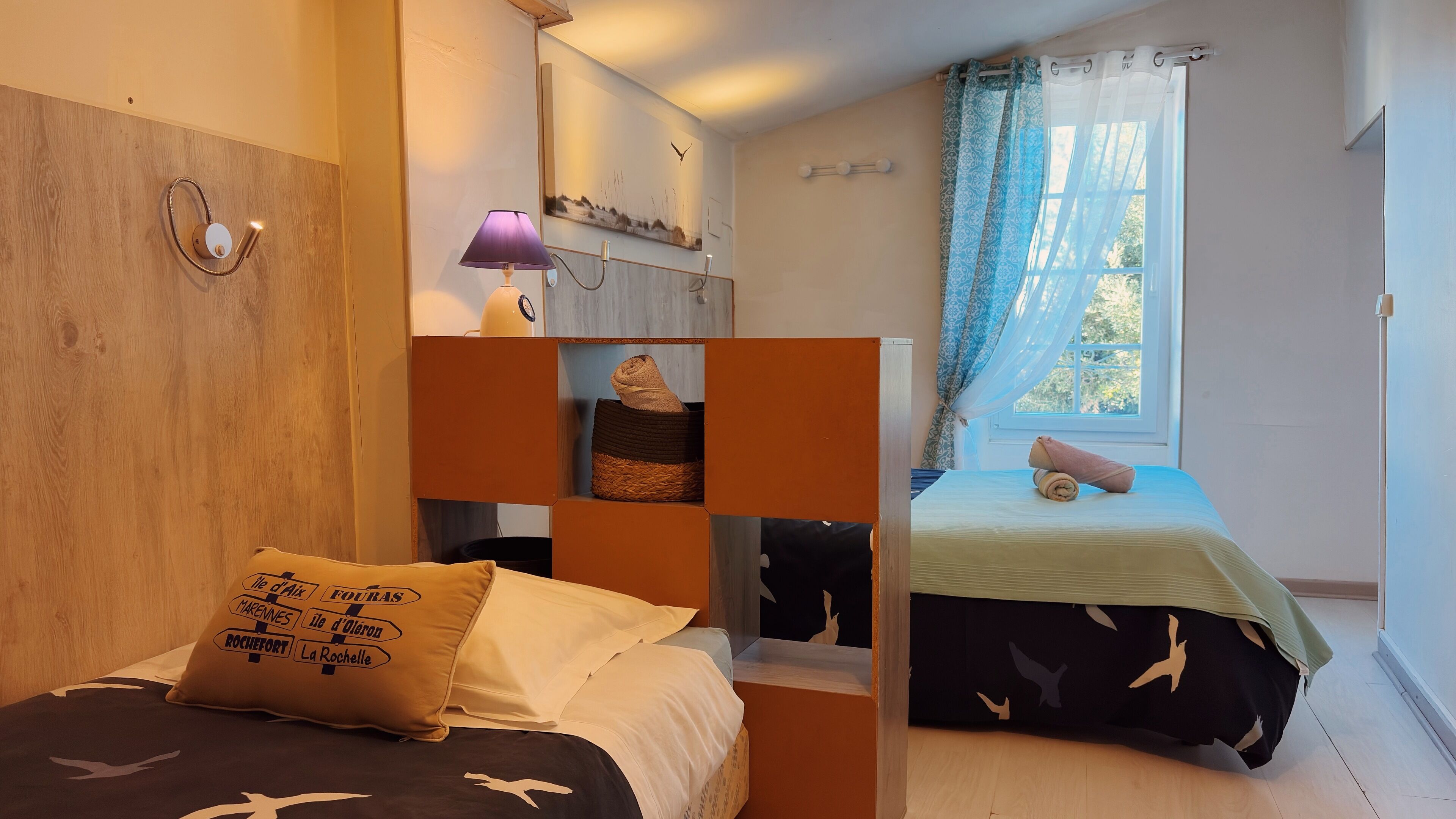 Una habitación con una cama, una mesita de noche, una lámpara, una ventana con cortinas y un estante en la pared con una toalla.