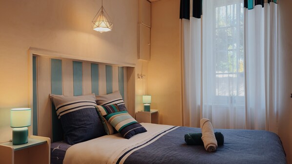 A neatly made bed with striped bedding, a bedside lamp, and a window with sheer curtains.