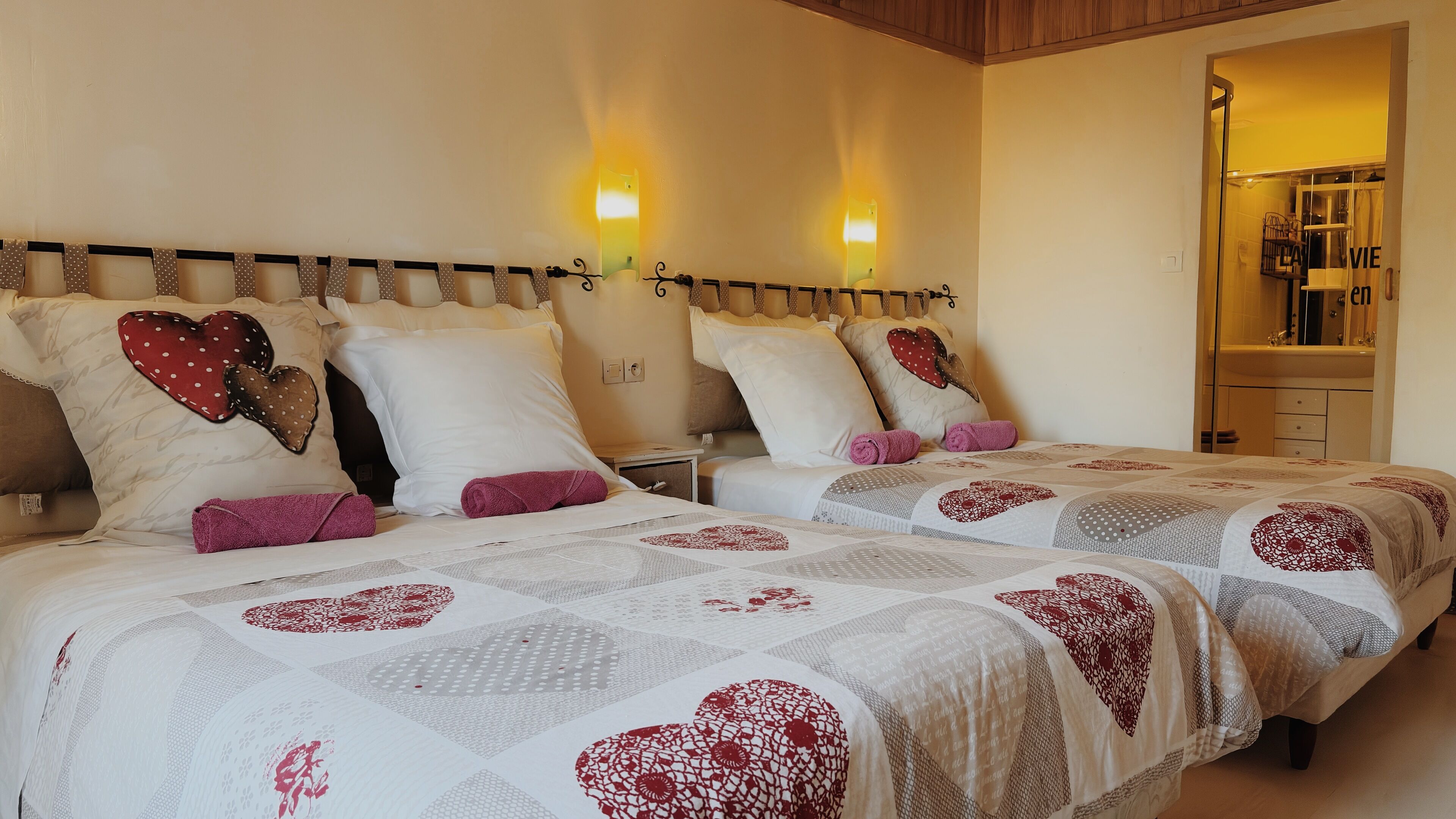 Habitación de hotel con dos camas, cada una con ropa de cama estampada con motivos de corazón y cabeceros con luces fijadas a la pared.