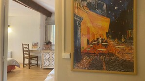 Une pièce comprenant un lit, une chaise, une table et un tableau représentant une scène de café.