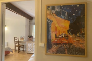 Une pièce comprenant un lit, une chaise, une table et un tableau représentant une scène de café.