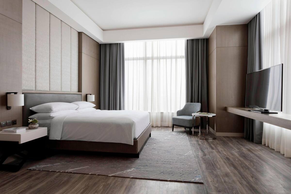 A modern hotel room with a large bed, a TV, a desk, and a chair.