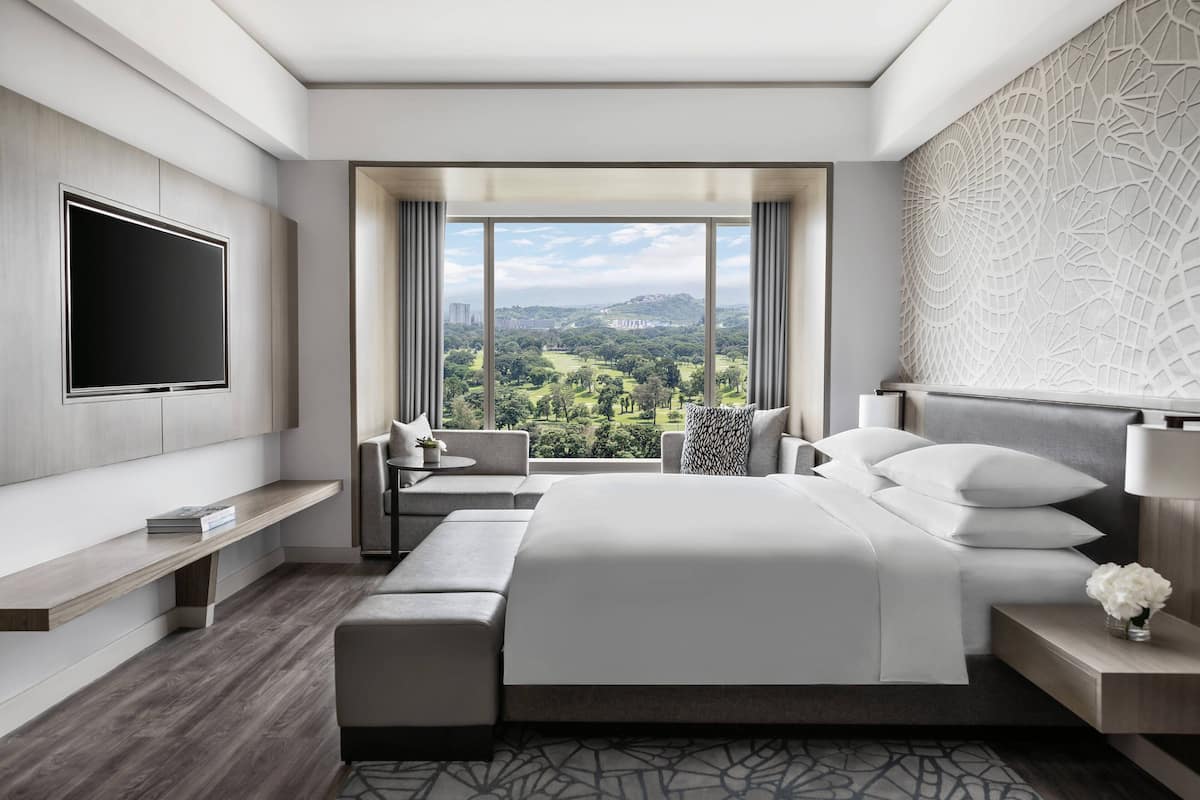 A modern hotel room with a large bed, a TV, a seating area with a view, and a decorative wall.