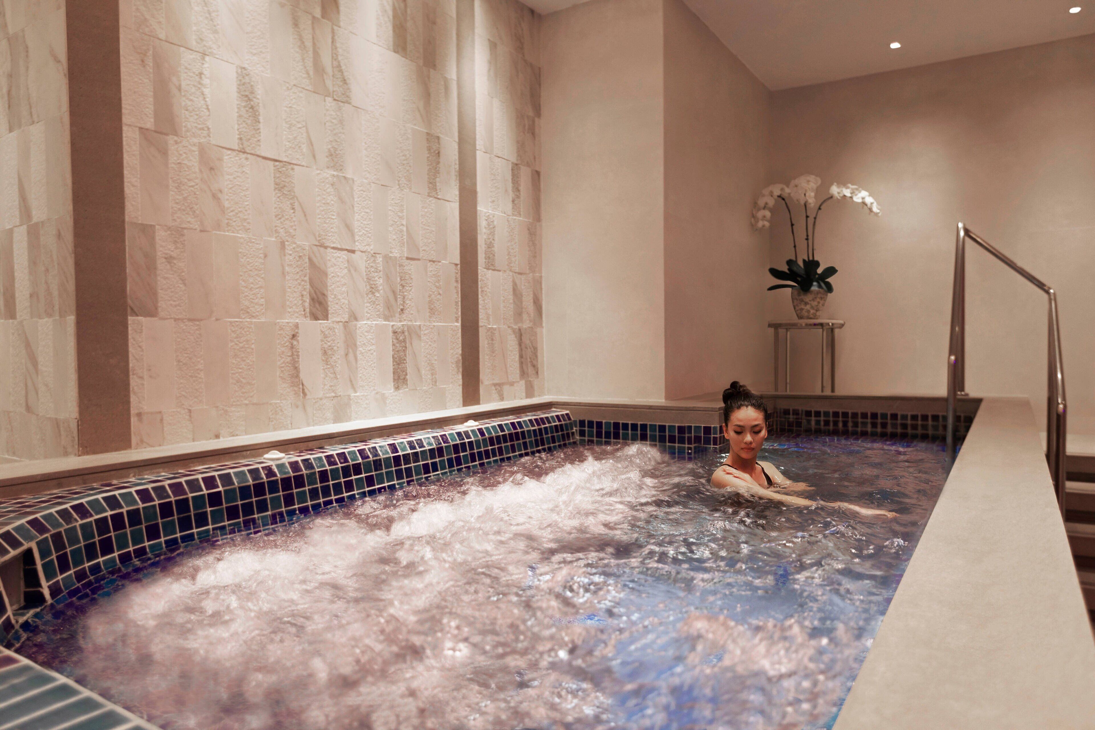 A spa area with a hot tub, tiled walls, and a potted plant.