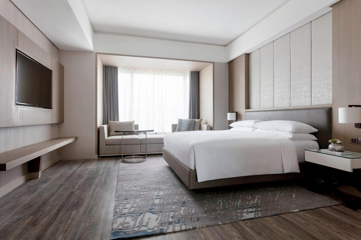 A modern hotel room with a large bed, a TV mounted on the wall, a sofa, and a small table.
