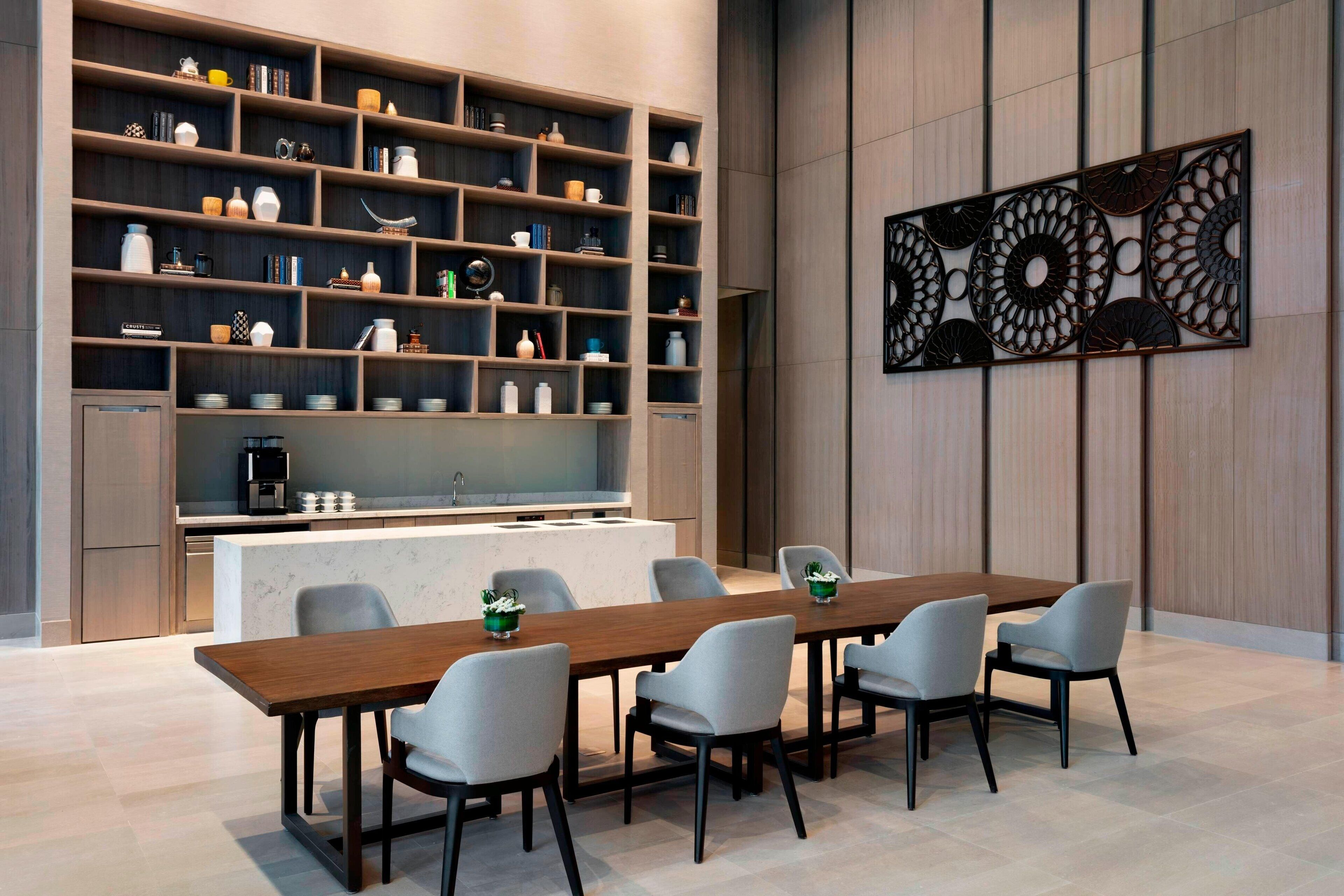 Una cocina moderna con comedor, que presenta una mesa de madera grande y sillas grises, rodeada de estanterías empotradas con diversos utensilios de cocina.