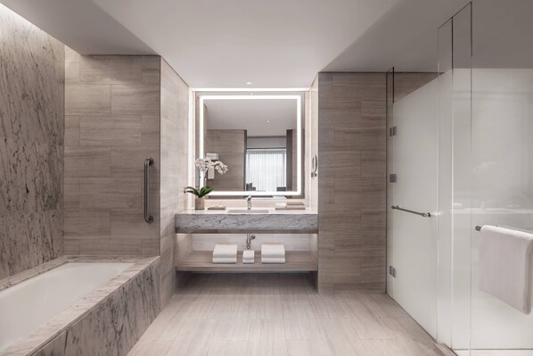 Un baño moderno con lavamanos de mármol, cabina de ducha de vidrio y tocador empotrado.