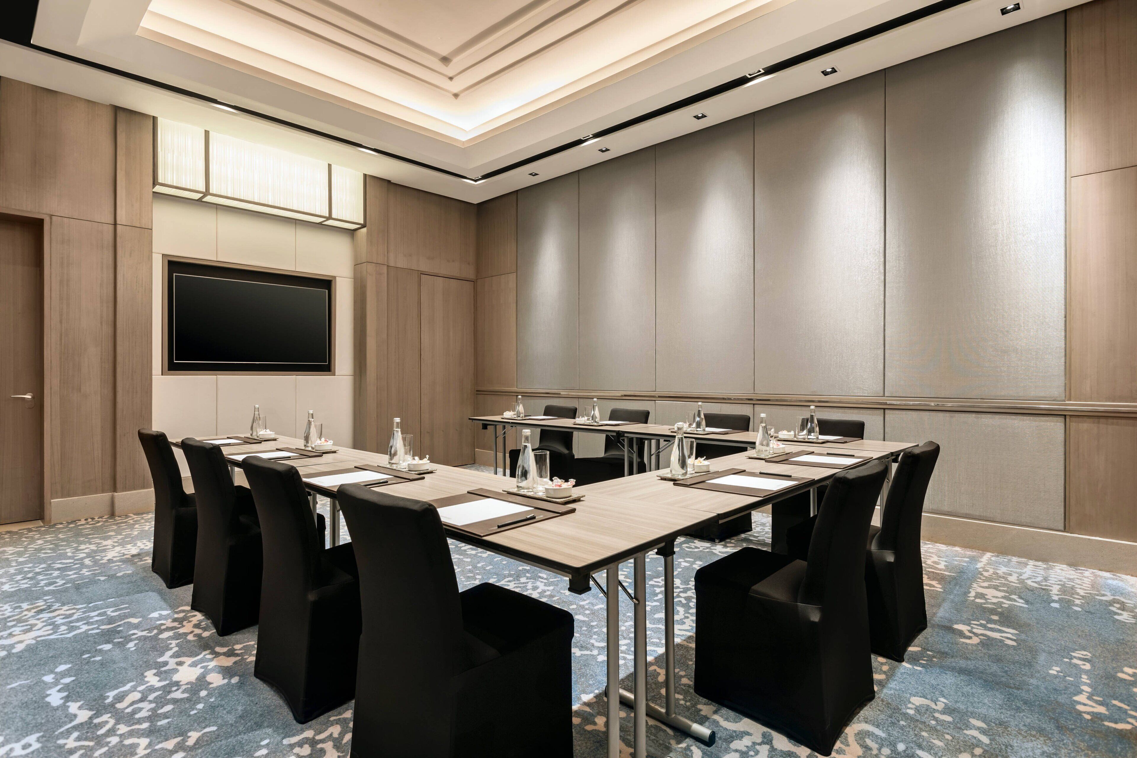 A conference room with a large flat-screen TV, multiple tables with chairs, and a blue patterned carpet.