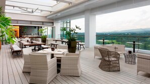 A spacious outdoor patio with wicker furniture, a bar area, and a view of the landscape. - Clark Marriott Hotel (Mabalacat City)