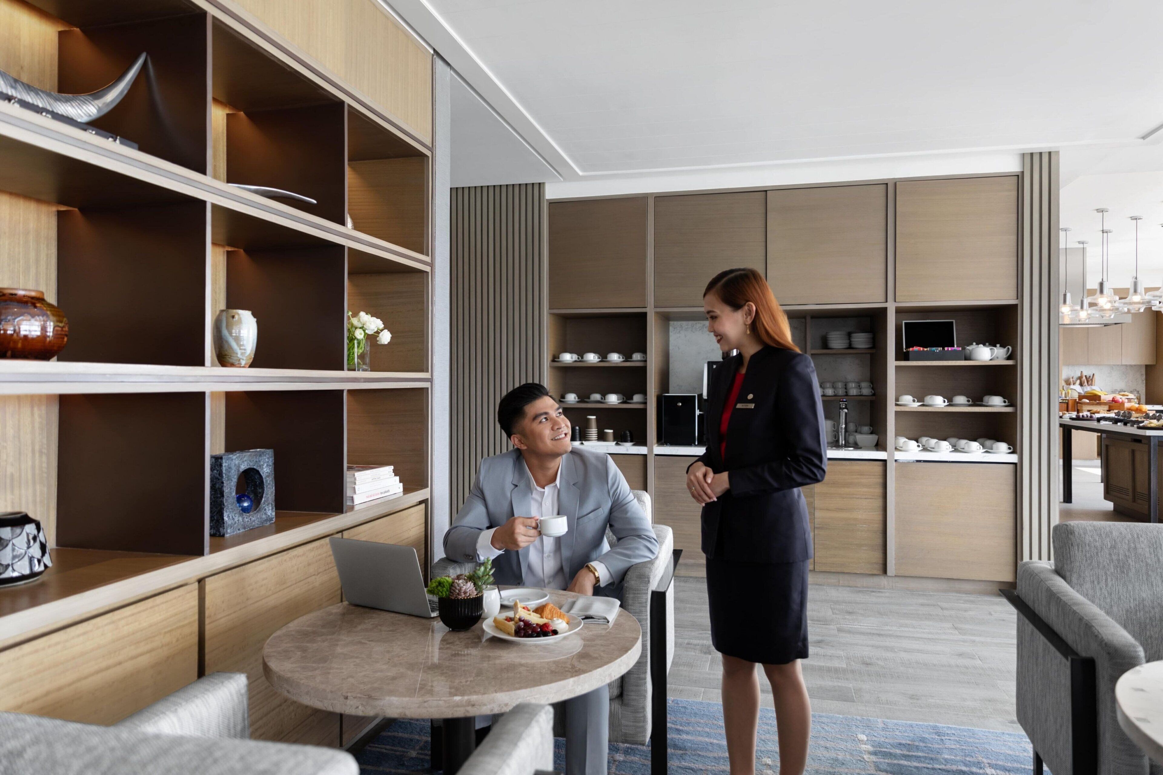 Una habitación de hotel moderna con comedor, una computadora portátil sobre una mesa y una persona de pie.