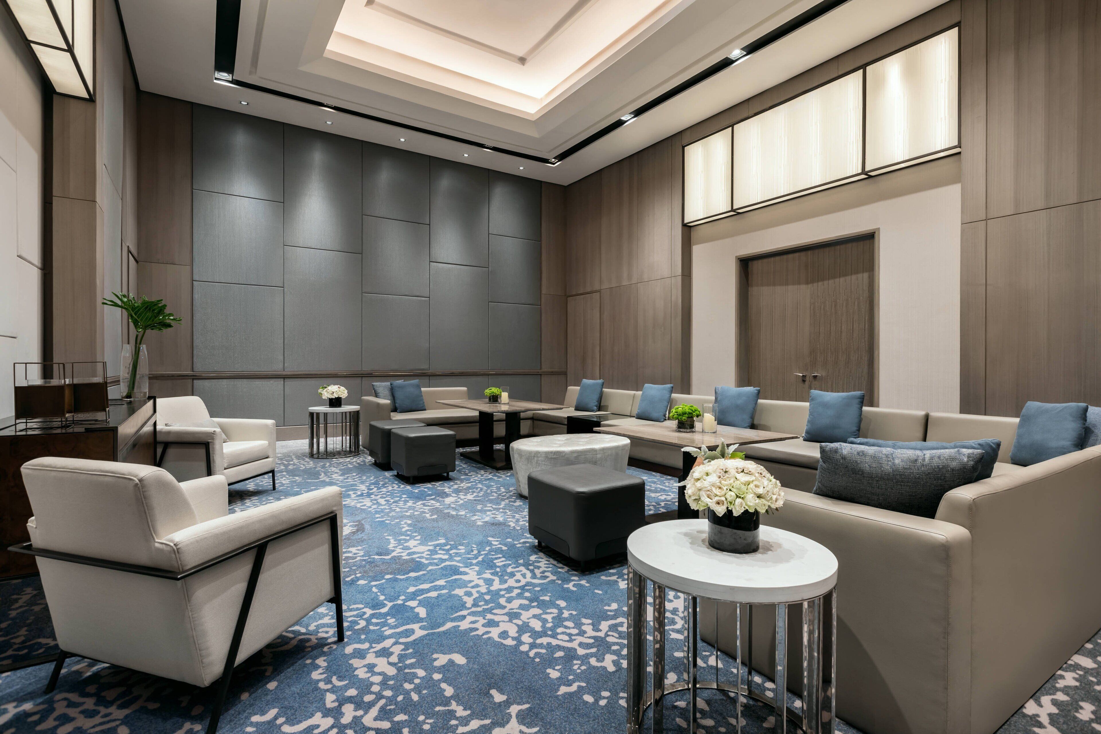 A modern hotel lobby with a large seating area, a reception desk, and a staircase.