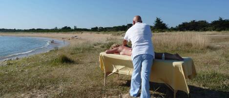 A beachside massage setup with a table and a person receiving a massage.