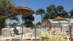 Area piscina con lettini e ombrelloni, circondata da alberi e un cielo sereno.